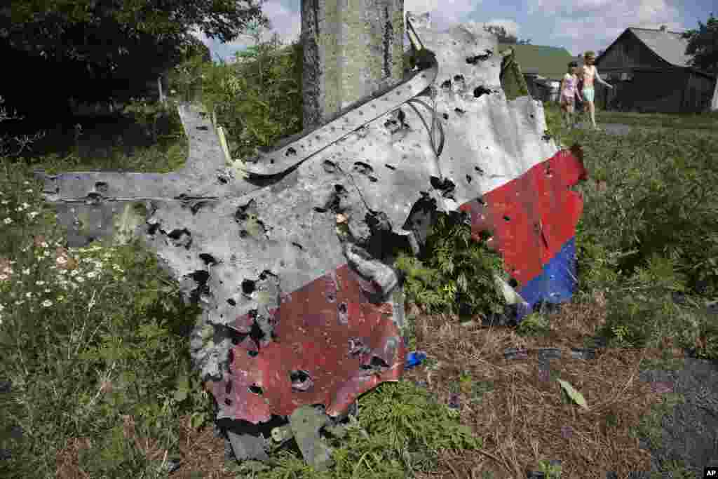 Children walk past a piece of wreckage from the Malaysia Airlines jet downed over Ukraine, in Petropavlivka village, Donetsk region, eastern Ukraine, July 23, 2014.