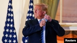 FILE - U.S. President Donald Trump pulls off his protective face mask as he poses atop the Truman Balcony of the White House.