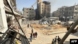 Palestinianos passam por edifícios danificados e destruídos em Beit Lahia, no norte da Faixa de Gaza, a 26 de outubro de 2024.