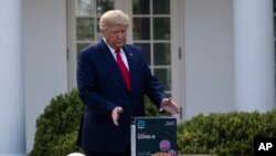 Presiden Donald Trump meraih sebuah kotak berisi tes cepat COVID-19 dari Abbott Laboratories, di Gedung Putih, Senin, 30 Maret 2020, di Washington. (Foto: AP / Alex Brandon)