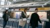 Orang-orang berjalan melintas di depan gerai maskapai penerbangan Jerman, Lufthansa, di Terminal 1, Bandara Internasional John F. Kennedy, di New York, 12 Maret 2020. (Foto: Kena Betancur/AFP)