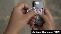 A mobile phone user in Juba, South Sudan removes his battery to check his SIM card, which had to be registered by February 28. (VOA)