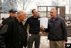 California Gov. Jerry Brown, second from left, looks at a students work book displayed by Interior Secretary Ryan Zinke, that was found during a tour of the fire ravaged Paradise Elementary School, Nov. 14, 2018, in Paradise, Calif. The school is among the thousands of homes and businesses destroyed along with dozens of lives lost when the fire burned through the area last week.