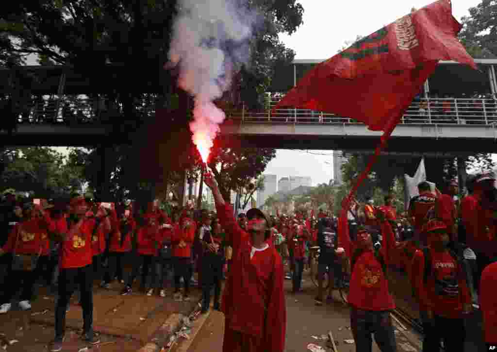 A worker lights up a flare during a May Day rally in Jakarta, Indonesia, Monday, May 1, 2017.