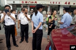 FILE - Yuan Shanshan, third right, the wife of detained Chinese lawyer Xie Yanyi, carries her child as she talks to a police officer while other plain clothes security personnel film journalists near the Tianjin No. 2 Intermediate People's Court in northern China.