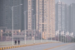 People wearing face masks walk down a deserted street in Wuhan in central China's Hubei Province, Jan. 28, 2020.