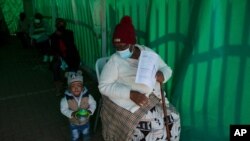 Seorang perempuan tua dengan seorang anak kecil mengantre untuk menerima vaksin Pfizer COVID-19 miliknya, di sebuah klinik di Orange Farm, dekat Johannesburg, Kamis, 3 Juni 2021. (Foto: AP)