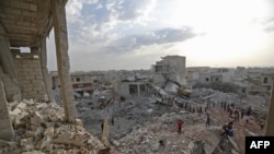 Warga Suriah berkumpul di tengah puing-puing bangunan yang hancur di Zardana, Idlib, Suriah yang sebagian besar dikuasai pemberontak, pasca serangan udara, 8 Juni 2018.