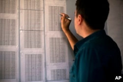 FILE - Bahzad Farhan Murad points to a list of missing and killed Yazidis in the small office where he collects evidence on Islamic State crimes against Yazidis, in Dohuk, Iraq, May 22, 2016.