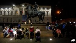 Residents sent running into the street after a magnitude-8.3 earthquake sit next to an equestrian statue in the main square of Santiago, Chile, Sept. 16, 2015.