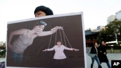 Seorang mahasiswi Korea Selatan memegang poster yang menggambarkan Presiden Korea Selatan Park Geun-hye (kanan bawah) sebagai boneka dan Choi Soon-sil, orang kepercayaannya, sebagai dalang, di Seoul (3/11).
