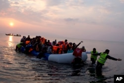 FILE - Volunteers help migrants and refugees on a dingy as they arrive at the shore of the northeastern Greek island of Lesbos, after crossing the Aegean Sea from Turkey, March 20, 2016.