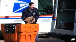 FILE - Seorang karyawan Layanan Pos Amerika Serikat mengangkat sebuah paket pos di luar kantor pos di Wheeling, Illinois, 29 Januari 2024.