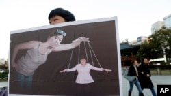 FILE - A South Korean college student holds a placard depicting South Korea's President Park Geun-hye, right bottom, as a marionette and Choi Soon-sil, who is at the center of a political scandal, as a puppeteer, in Seoul, South Korea.