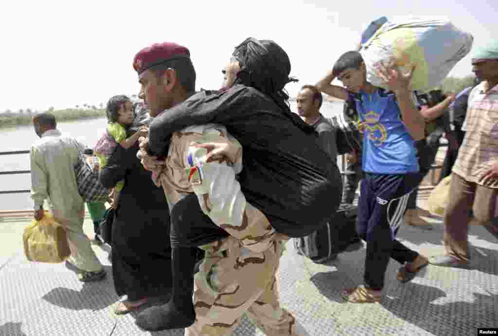 A member of Iraqi security forces carries an elderly woman across a bridge on the outskirts of Baghdad, May 24, 2015.