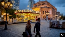 People wearing face masks walk past a carousel and the Old Opera in Frankfurt, Germany, Wednesday, Oct. 28, 2020. To avoid the further outspreads of the Coronavirus new restriction will be valid from next Monday. (AP Photo/Michael Probst)