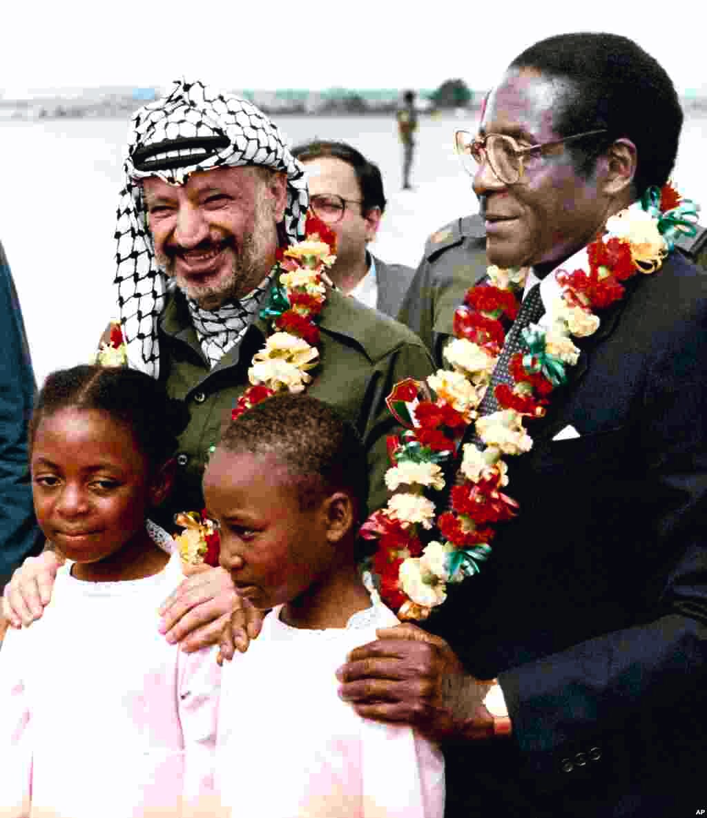 Zimbabwean Prime Minister Robert Mugabe, right, and Yasser Arafat, left, pose for photos after being garlanded by two 10-year-old school girls, Jean Chitanda, left, and Tsitsi Chikasha, on Arafat's arrival at Harare Airport, Zimbabwe, April 14, 1987, to attend a meeting of the Non-aligned Movement's Committee on Palestine.