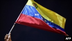 Un hombre muestra una bandera nacional mientras familiares y amigos de migrantes venezolanos que murieron cuando se hundió un barco que los transportaba a Trinidad y Tobago, protestan en Güiria, Venezuela, el 18 de diciembre de 2020.