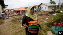 Seorang perempuan migran Rohingya membawa tumpukan piring kotor untuk dicuci di tempat penampungan di Kuala Langsa, Aceh (25/5). (AP/Tatan Syuflana)