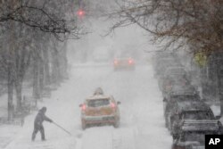 Seorang pria membersihkan jalanan dari salju dengan menggunakan sekop di tengah lalu lintas di 81st street, 4 Januari 2018, di Upper East Side, Manhattan.