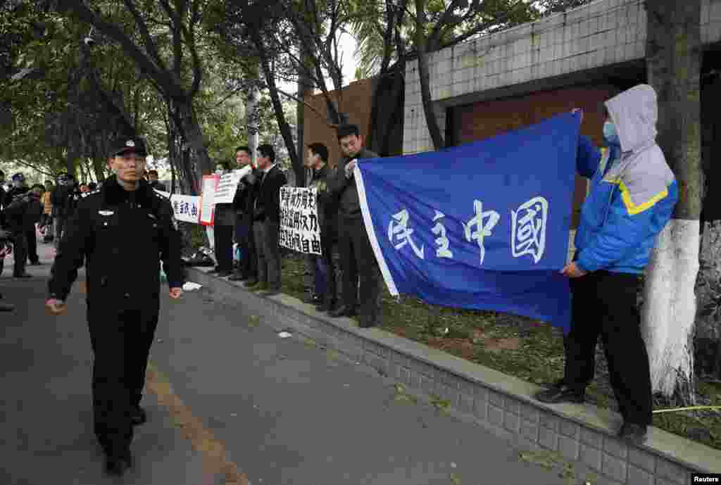 2013年1月9日,一名警察走过在广州市《南方周末》总部外面举着支持《南周》横幅的抗议人群。