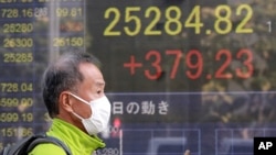 A man walks by an electronic stock board of a securities firm in Tokyo, Wednesday, Nov. 11, 2020. Shares were mostly higher Wednesday in Asia after a worldwide rally spurred by hopes that a COVID-19 vaccine will help the global economy return to…