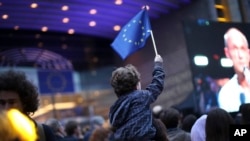 Seorang anak lelaki melambaikan bendera Uni Eropa seraya menonton layar televisi lebar di luar gedung Parlemen Eropa di Brussels, Belgia, 26 Mei 2019 (foto: AP Photo/Fransisco Seco)