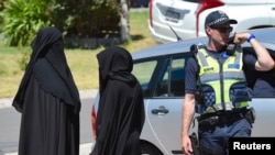 Dua perempuan berdiri dekat polisi yang memblokir jalan di tengah penggeledahan sebuah rumah di Meadow Heights, pinggiran kota Melbourne, Australia (23/12). 