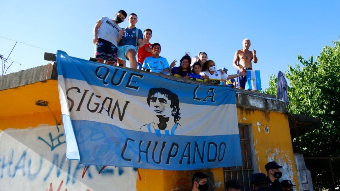 Fans stand on a roof of a house along the route of the motorcade carrying the remains of football star Diego Maradona to the Jardin de Bellavista cemetery in Buenos Aires, Argentina, Nov. 26, 2020. 