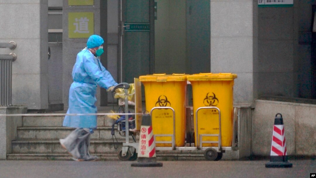 Staff move bio-waste containers past the entrance of the Wuhan Medical Treatment Center, where some infected with a new virus are being treated, in Wuhan, China, Wednesday, Jan. 22, 2020. (AP Photo/Dake Kang)