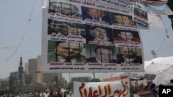 Egyptian protesters walk under a big banner with pictures of some journalists. It reads 'The military council protects the former regime.' Another banner calls for 'Media purification,' Tahrir Square, Cairo, Egypt, July 10, 2011