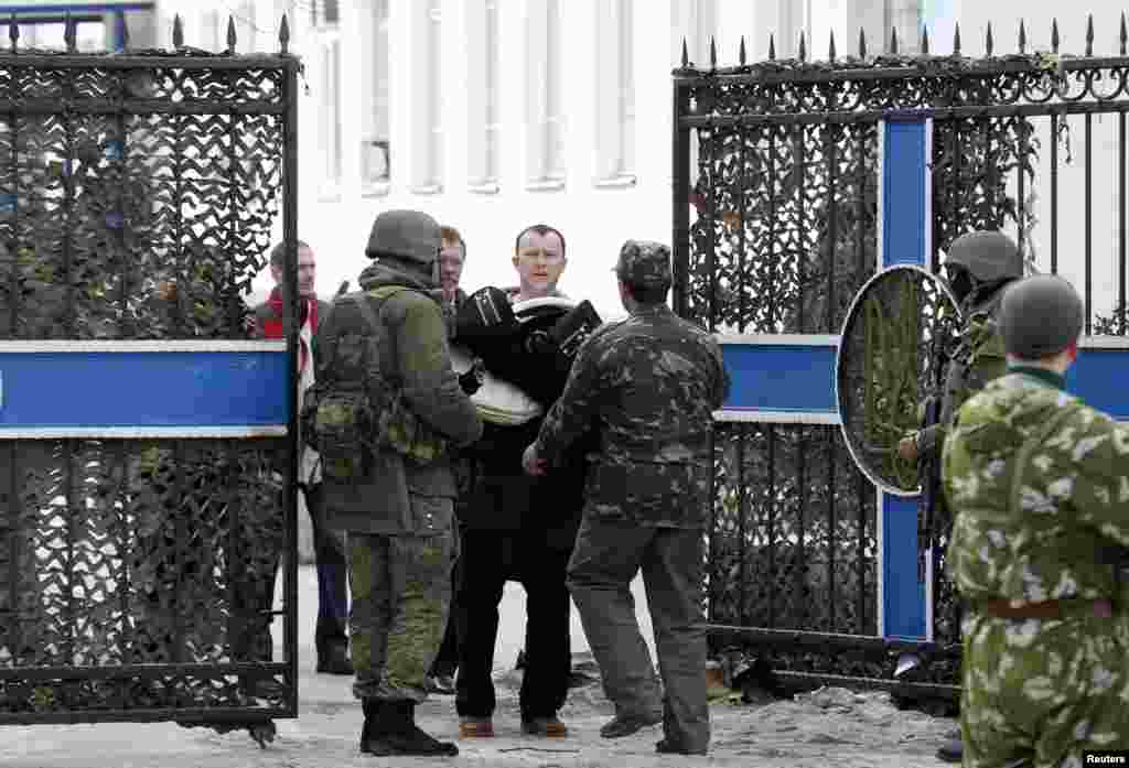 Seorang pejabat angkatan laut Ukraina membawa barang-barangnya keluar dari markas angkatan laut di Sevastopol, Ukraina, diawasi oleh pria-pria bersenjata yang diyakini sebagai tentara Rusia (19/3).