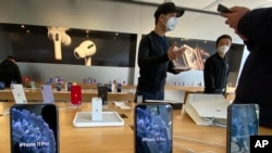In this photo taken Wednesday, Feb. 19, 2020, staff chats with customers at an apple store in Beijing. Factories that make the world's smartphones, toys and other goods are struggling to reopen after a virus outbreak idled China's economy. But even…