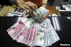 Seorang teller di money changer menunjukkan Rupiah Indonesia dan dolar AS di Jakarta. Presiden Joko Widodo berkomitmen untuk membayar piutang rakyat dan swasta yang telah berkekuatan hukum tetap atau inkrah. (Foto: Reuters)