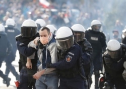 Polish police in riot gear detain protesters angry over new restrictions aimed at fighting the coronavirus pandemic, in Warsaw, Oct. 24, 2020.