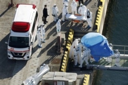 Officers in protective gear escort a person (under the blue sheet) who was aboard cruise ship Diamond Princess and tested positive for coronavirus, after the person is transferred to a maritime police base in Yokohama, Japan, Feb. 4, 2020.
