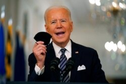 President Joe Biden holds up his face mask as he speaks about the COVID-19 pandemic during a prime-time address from the East Room of the White House, March 11, 2021.