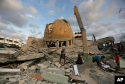 Beberapa warga berdiri di luar sebuah masjid yang hancur akibat serangan udara Israel di kota Khan Younis, Jalur Gaza, Minggu, 8 Oktober 2023.