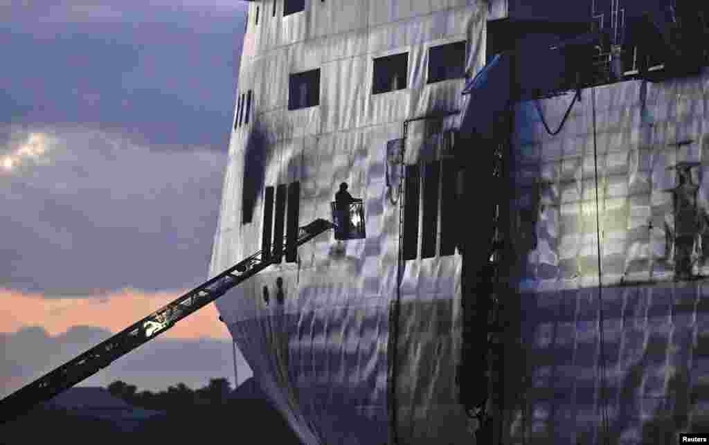 Petugas pemadam kebakaran berdiri di tangga untuk memeriksa dek mobil dan truk kapal feri Norman Atlantic yang berlabuh di pelabuhan Brindisi, 2 Januari 2015. 