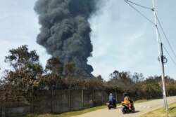 Pengendara motor melewati kepulan asap pekat akibat kebakaran kilang Balongan milik PT Pertamina, Indramayu,Jawa Barat, 29 Maret 2021. Ratusan orang dievakuasi dari desa terdekat setelah kebakaran besar terjadi di kilang tersebut. (Foto AP)