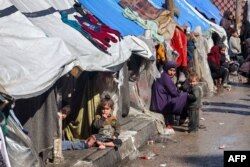 Seorang perempuan dan anak-anak duduk di luar tenda yang menampung pengungsi Palestina di Rafah di Jalur Gaza selatan pada 8 Februari 2024. (Foto: AFP)