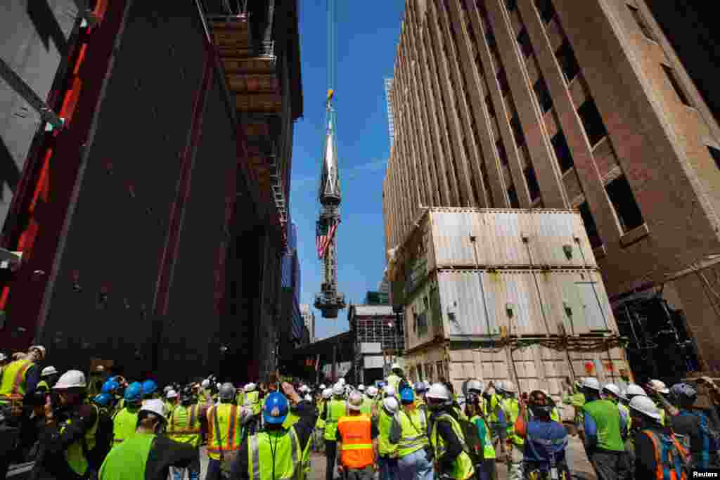 Members of the media and workers at the Ground Zero site watch as one of the last two segments of the silver spire is lifted to the top of One World Trade Center, May 2, 2013.