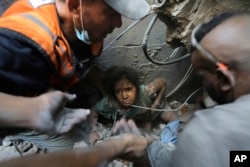 Sejumlah petugas SAR berusaha menyelamatkan seorang anak perempuan dari puing-puing sebuah gedung yang dihancurkan oleh serangan udara Israel di kamp Jabaliya, di utara Jalur Gaza, 1 November 2023. (Foto: Abed Khaled/AP Photo)