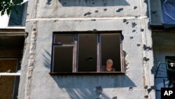 Seorang perempuan melongok ke luar jendela apartemennya di sebuah bangunan yang rusak akibat serangan roket pada Mei lalu, di Sloviansk, wilayah Donetsk, timur Ukraina, Sabtu, 6 Agustus 2022.