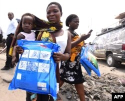 FILE - A woman carrying a baby holds a treated mosquito net.
