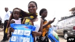 FILE - A woman carrying a baby holds a treated mosquito net during a malaria prevention action at Ajah in Eti Osa East district of Lagos, Nigeria, April 21, 2016.