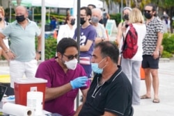 FILE - Carlos Anacleto closes his eyes as he receives the Pfizer COVID-19 vaccine from nurse Jorge Tase, as others wait their turn, Aug. 4, 2021, in Miami Beach, Fla.