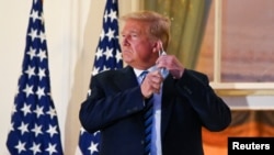 U.S. President Donald Trump pulls off his protective face mask as he poses atop the Truman Balcony of the White House after returning from being hospitalized at Walter Reed Medical Center for coronavirus disease (COVID-19) treatment, in Washington, U.S. O