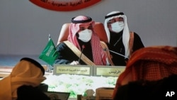روزنامه نگاران در حال تماشای تصویری بزرگ از محمد بن سلمان، ولیعهد عربستان سعودی، در کرسی ریاست نشست شورای همکاری خليج فارس، هستند. ۵ ژانویه ۲۰۲۱