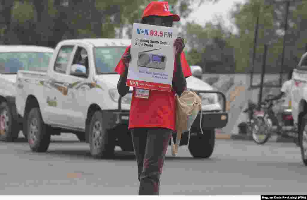 The launch of the 93.5 Voice of America station is... great news for all of us South Sudanese. We need our news and events to be going out to other people. - Chubarex from Juba A young woman braves the traffic in Juba, South Sudan, with a poster advertising the launch of Voice of America's new FM transmitter. The transmitter, which was ceremoniously launched on Thursday, March 21, 2013, joins a network that bring Voice of Americ